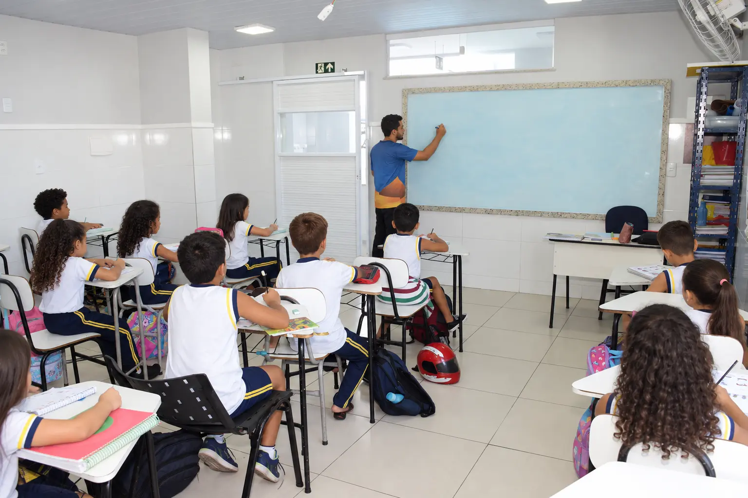 Professor do Colégio Millennium escrevendo no quadro para a turma de farda branca e azul